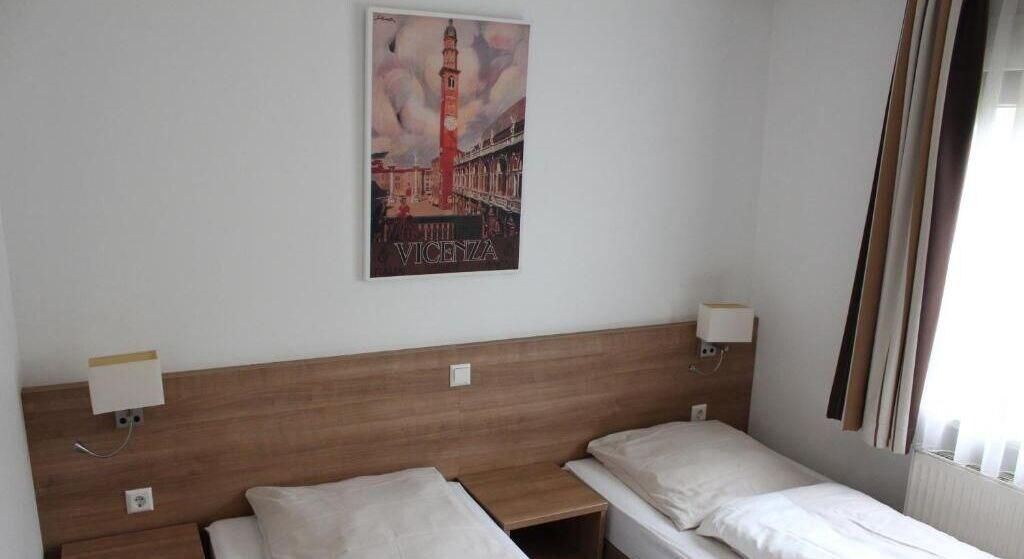 A hotel room with two single beds, a wooden headboard, a wall-mounted poster of a tower, and a window with curtains.