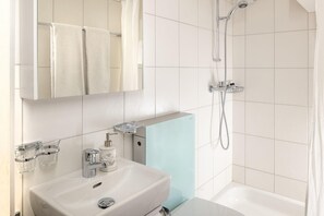 Un baño con lavamanos blanco, un espejo, ducha y toallero.