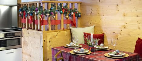Un coin repas agrémenté d'une cloison en bois décorée d'ornements de Noël, d'une nappe à carreaux et d'une bougie posée sur la table.