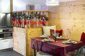 Un comedor con un separador de madera decorado con adornos navideños, mantel a cuadros y una vela sobre la mesa.