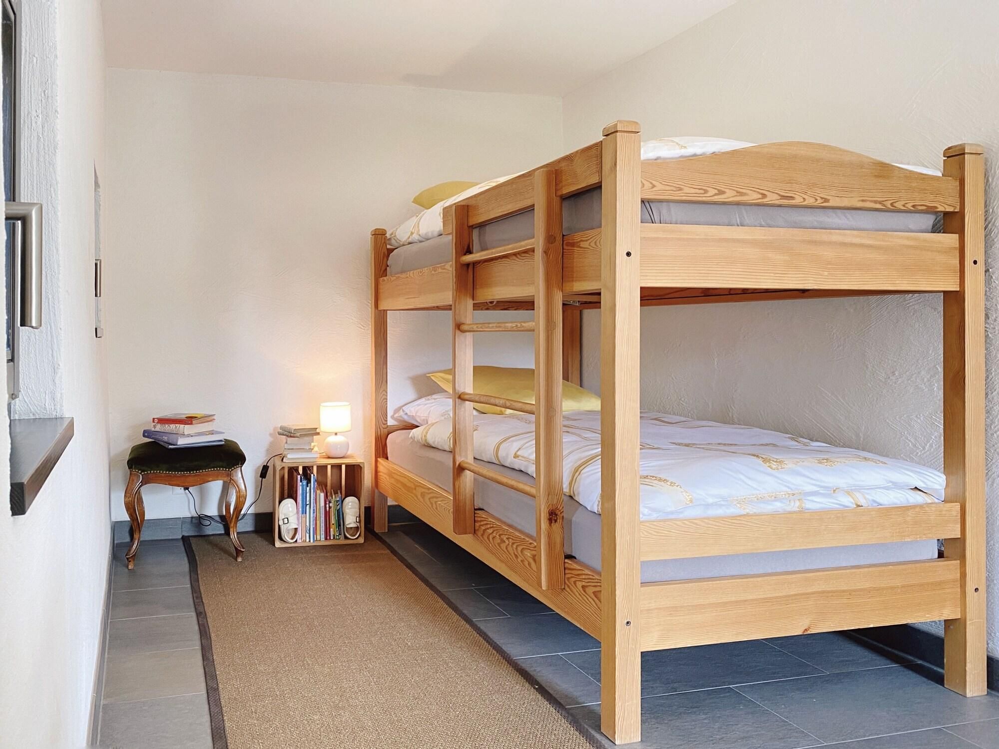 A bunk bed with a wooden frame, a bedside table with a lamp, and a small chair.