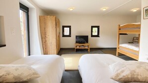 Une chambre avec deux lits, une armoire en bois, un téléviseur posé sur un meuble et deux fenêtres.