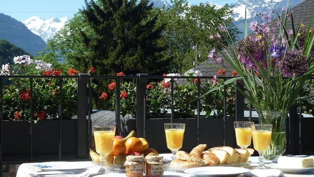 Une table dressée avec des aliments pour le petit-déjeuner, notamment des croissants, des fruits et du jus, avec une vue sur les montagnes en arrière-plan.