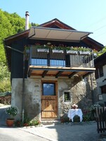 Un edificio di due piani con un balcone in legno, un camino e una facciata in pietra.