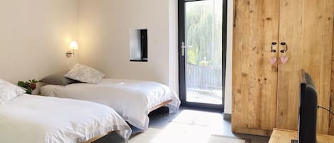 A bedroom with two beds, a wooden wardrobe, a television, and a window with a view of greenery.