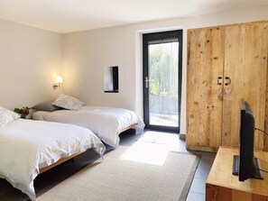 Un dormitorio con dos camas, un armario de madera, una televisión y una ventana con vistas a la vegetación.