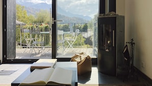 Une pièce dotée d’une grande porte-fenêtre coulissante donnant sur un balcon avec vue sur les montagnes et la verdure.