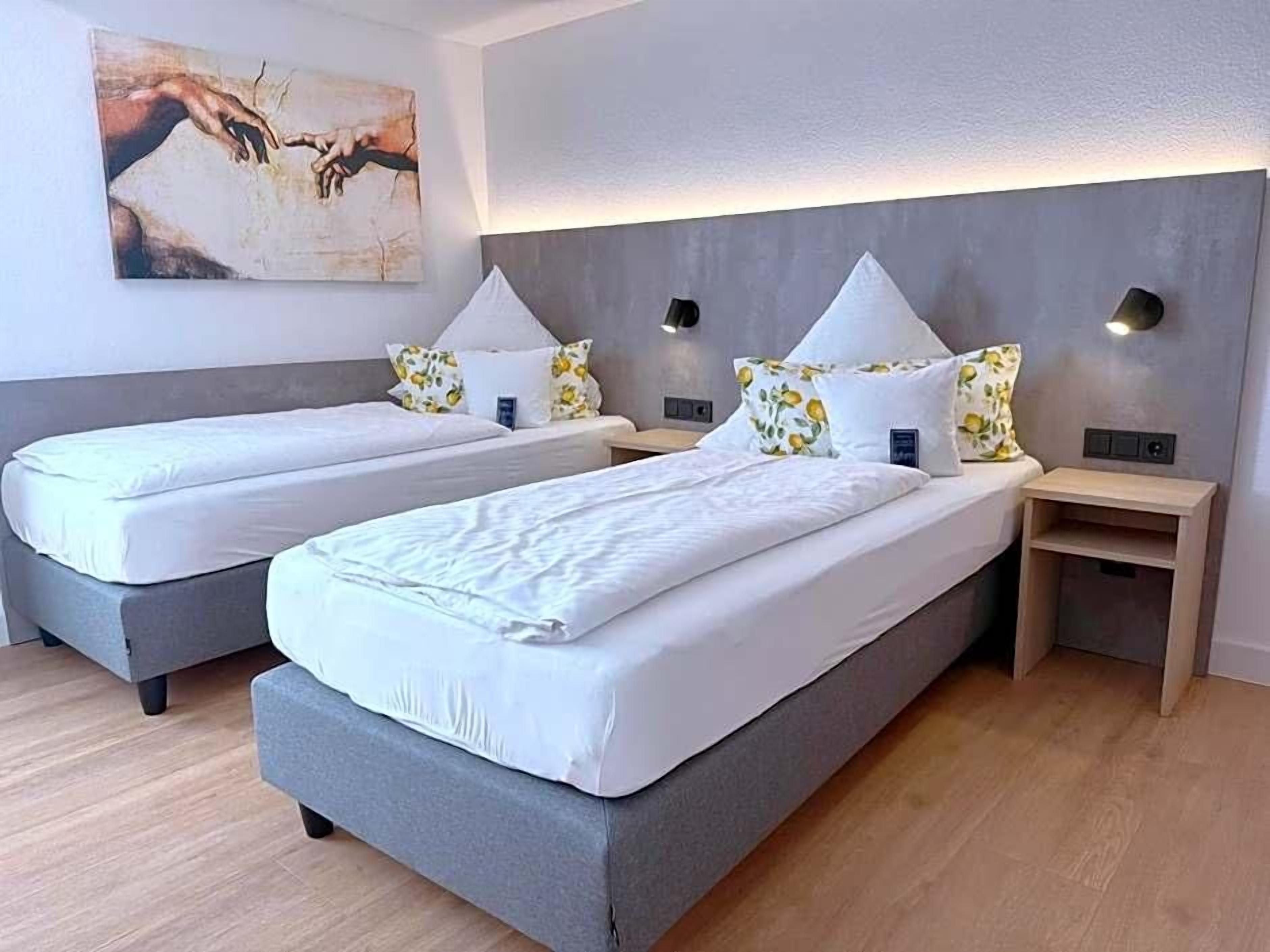 A hotel room with two beds, a painting on the wall, and a small wooden side table.