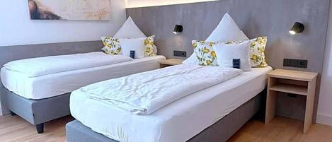 Habitación de hotel con dos camas, un cuadro en la pared y una mesita de madera.