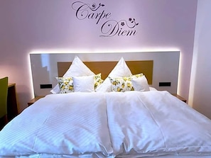 A neatly made bed with white linens and floral pillows, a headboard with a light fixture, and a wall sign that reads 'Carpe Diem'. - Hotel Restaurant Thum (Balingen)