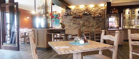 Interior de restaurante con pared de piedra, mobiliario de madera y una zona de bar.