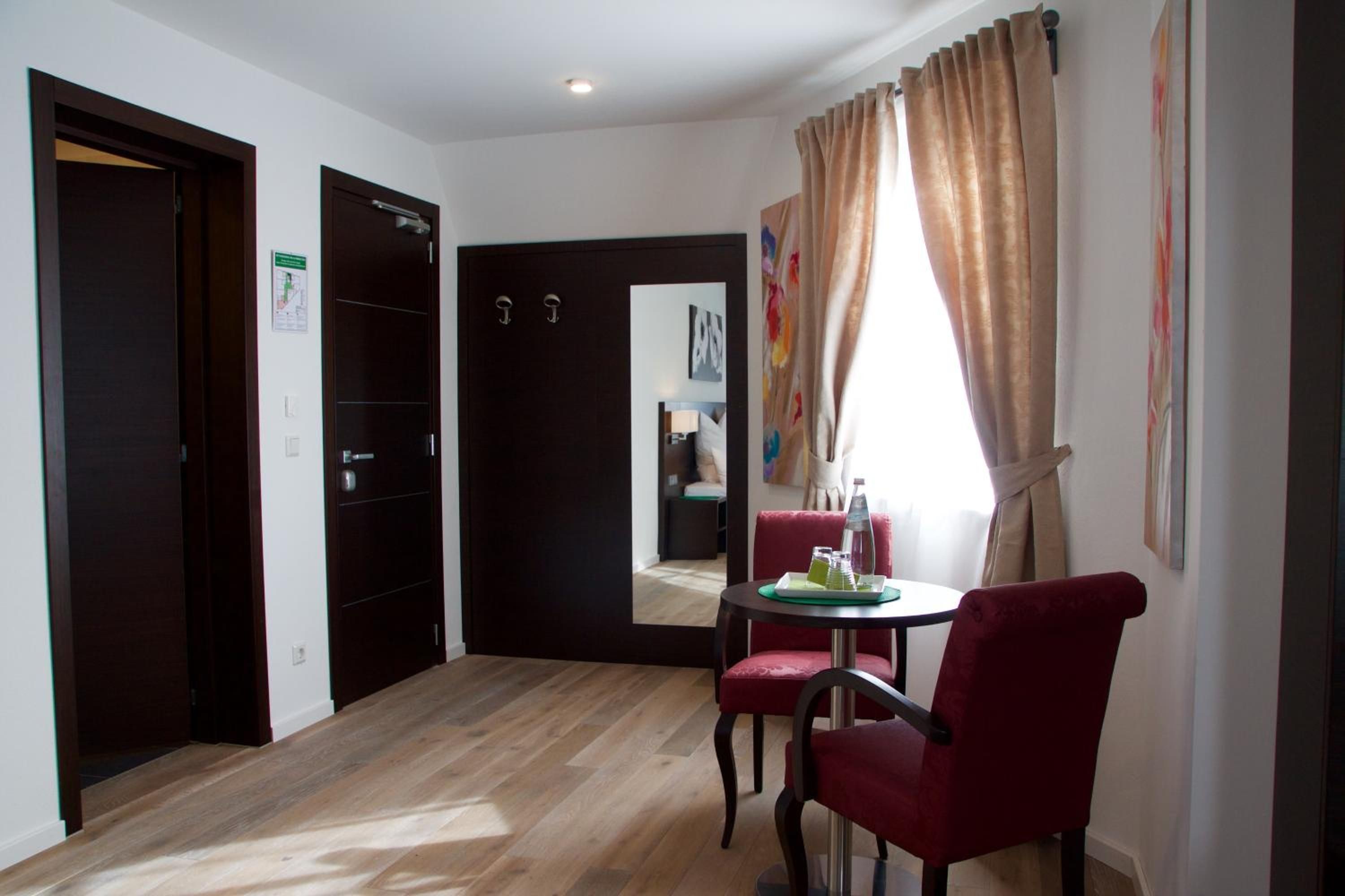 Une chambre d’hôtel avec un plancher en bois, une table à manger avec des chaises, un miroir et une fenêtre avec des rideaux.
