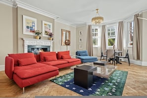 A living room with a fireplace, a red sofa, a blue armchair, and a chandelier. - Holland Park 5BR 3BA Stay With Private Sauna (London)