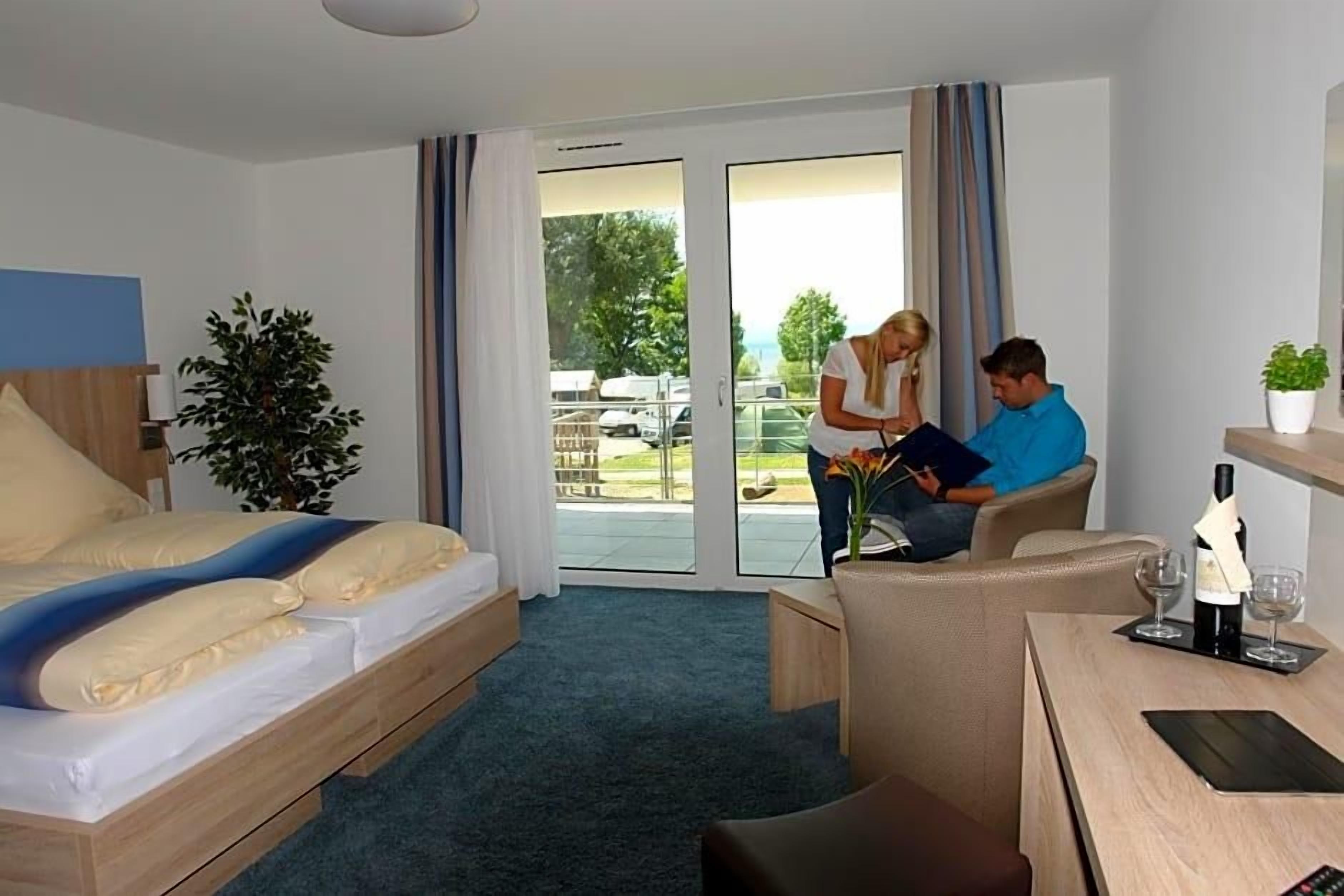 Ein Hotelzimmer mit Bett, Schreibtisch, Stuhl, Pflanze und Blick ins Freie.