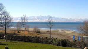 Un paysage côtier avec un ciel dégagé, une plage de sable et une chaîne de montagnes à l’horizon.