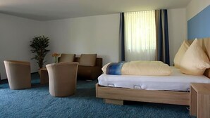 Une chambre d’hôtel avec un lit, deux canapés, une petite table et une plante en pot.