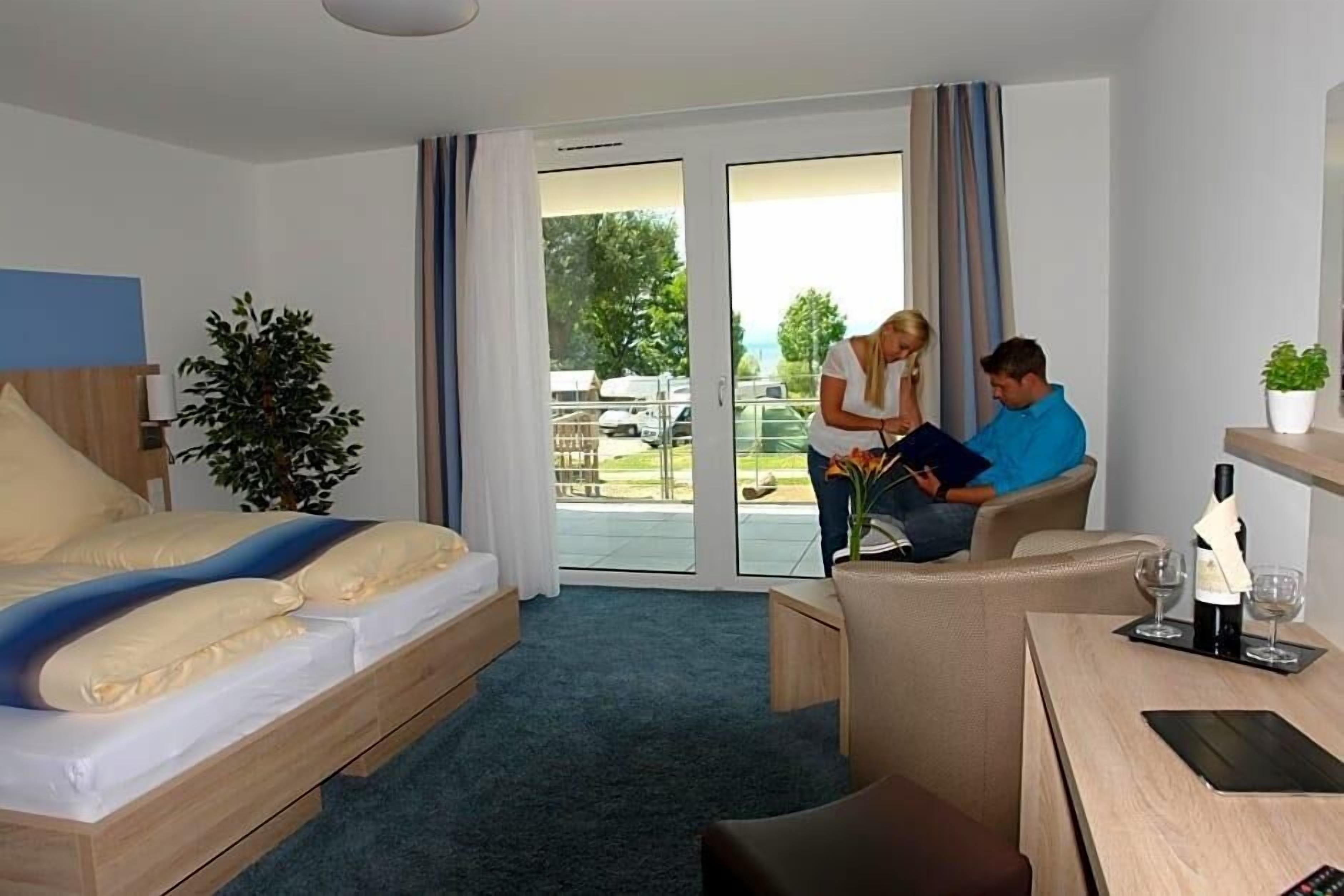 Camera d'albergo con un letto, una scrivania, una sedia, una pianta e vista sull'esterno.