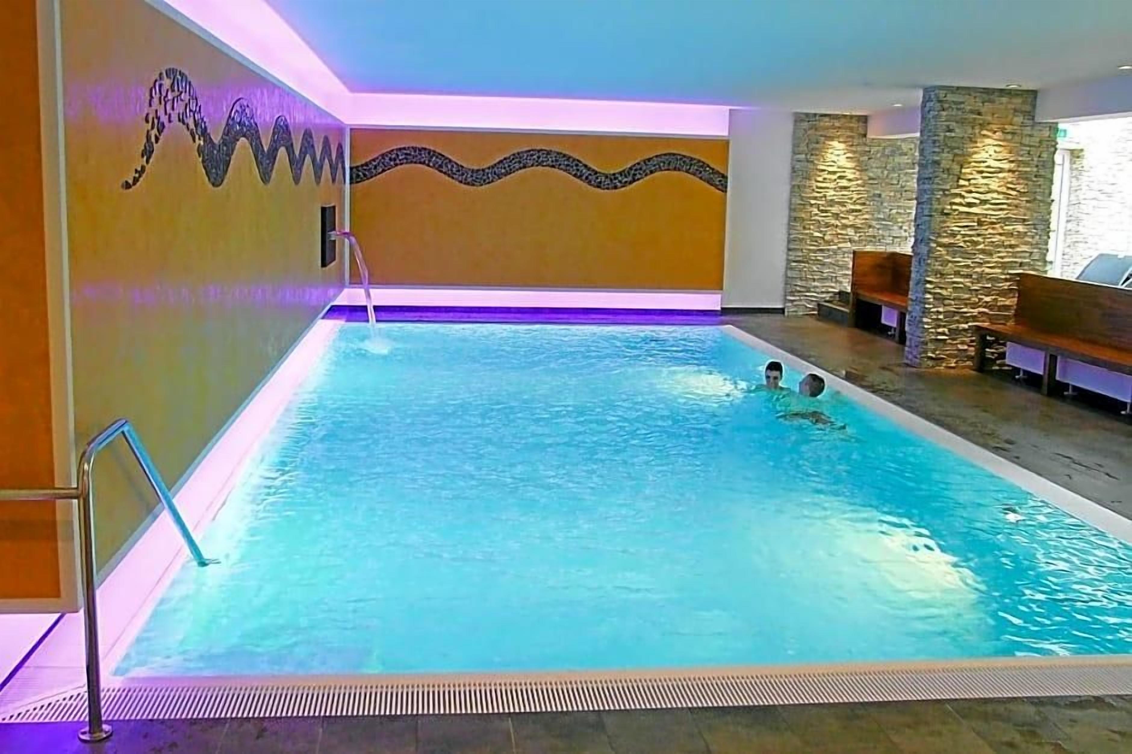 Una piscina interior con un diseño de pared ondulada, paredes de piedra y zonas de estar.