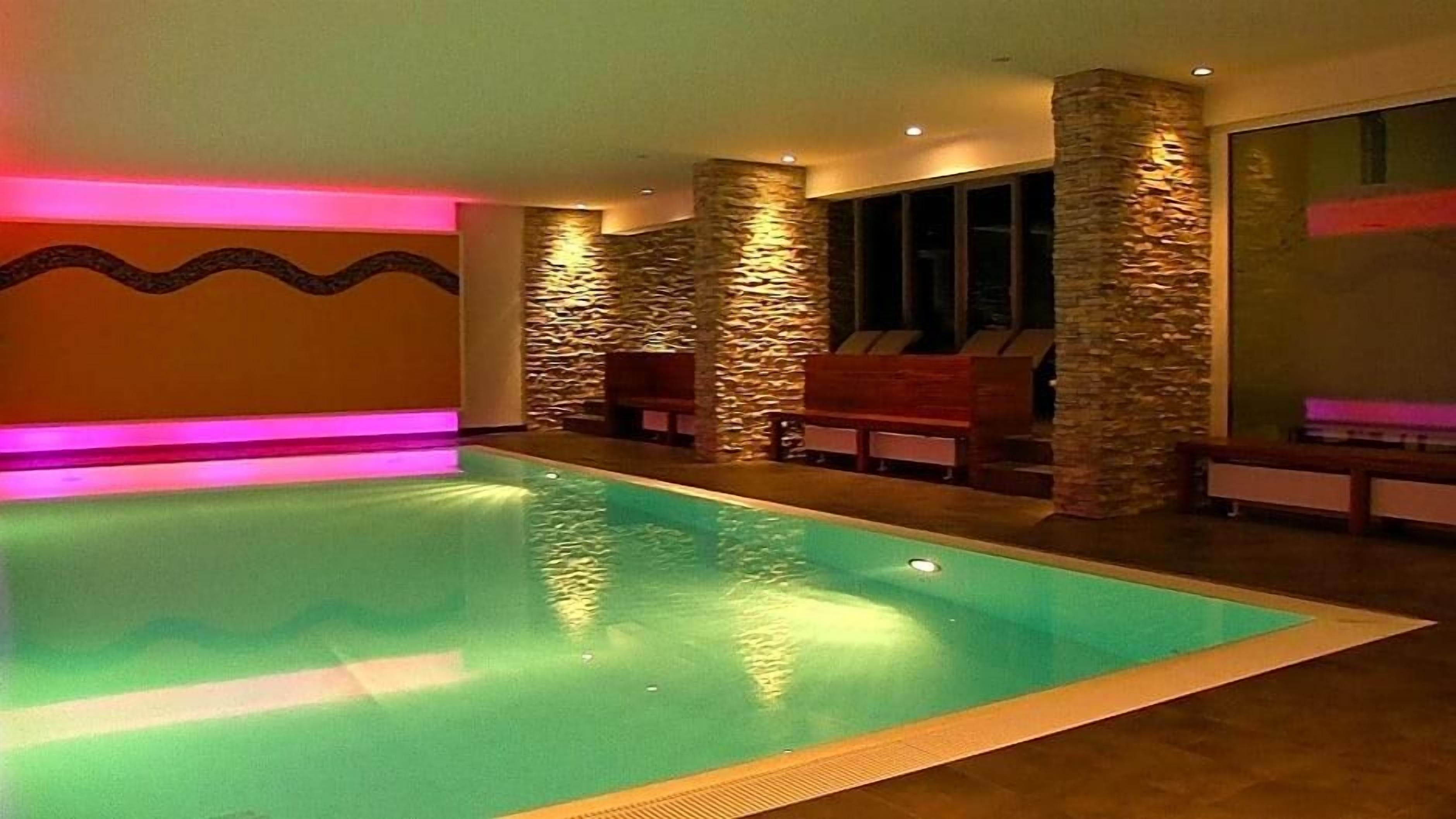 An indoor swimming pool with stone pillars, benches, and a wavy wall design.