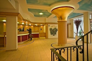 Eine Hotelhalle mit einer Rezeption, einer großen Säule und einer Treppe.