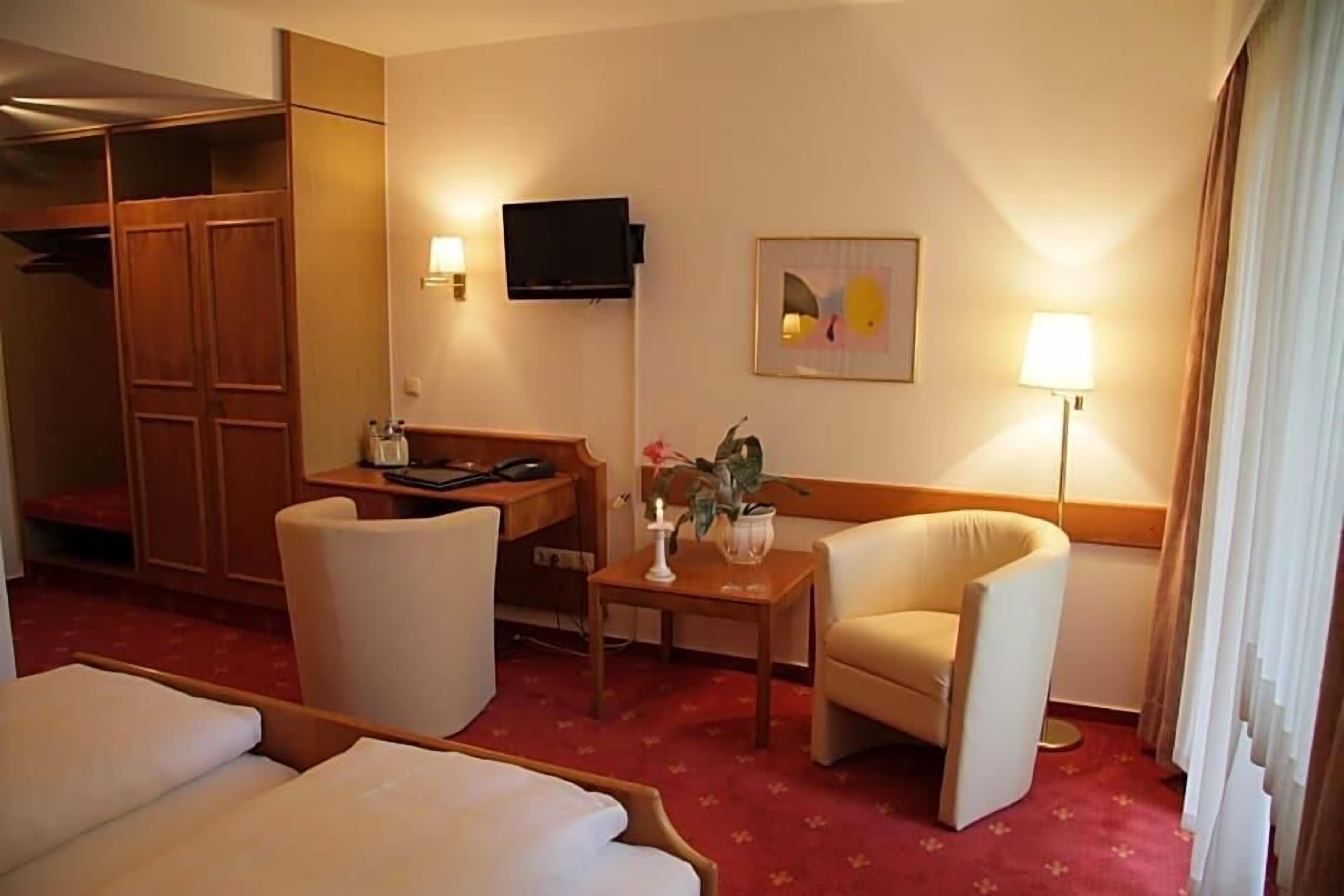 Ein Hotelzimmer mit einem Bett, zwei Sesseln, einem Schreibtisch, einem Fernseher und einer Lampe.
