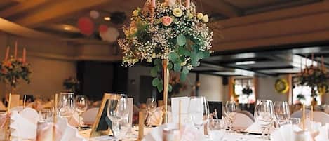 Une table de banquet dressée avec des serviettes blanches, des assiettes décoratives dorées et de la verrerie transparente.