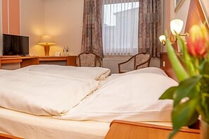 A hotel room with a bed, a television, a nightstand, a lamp, and a window with curtains. - Hotel Daub (Bremervörde)