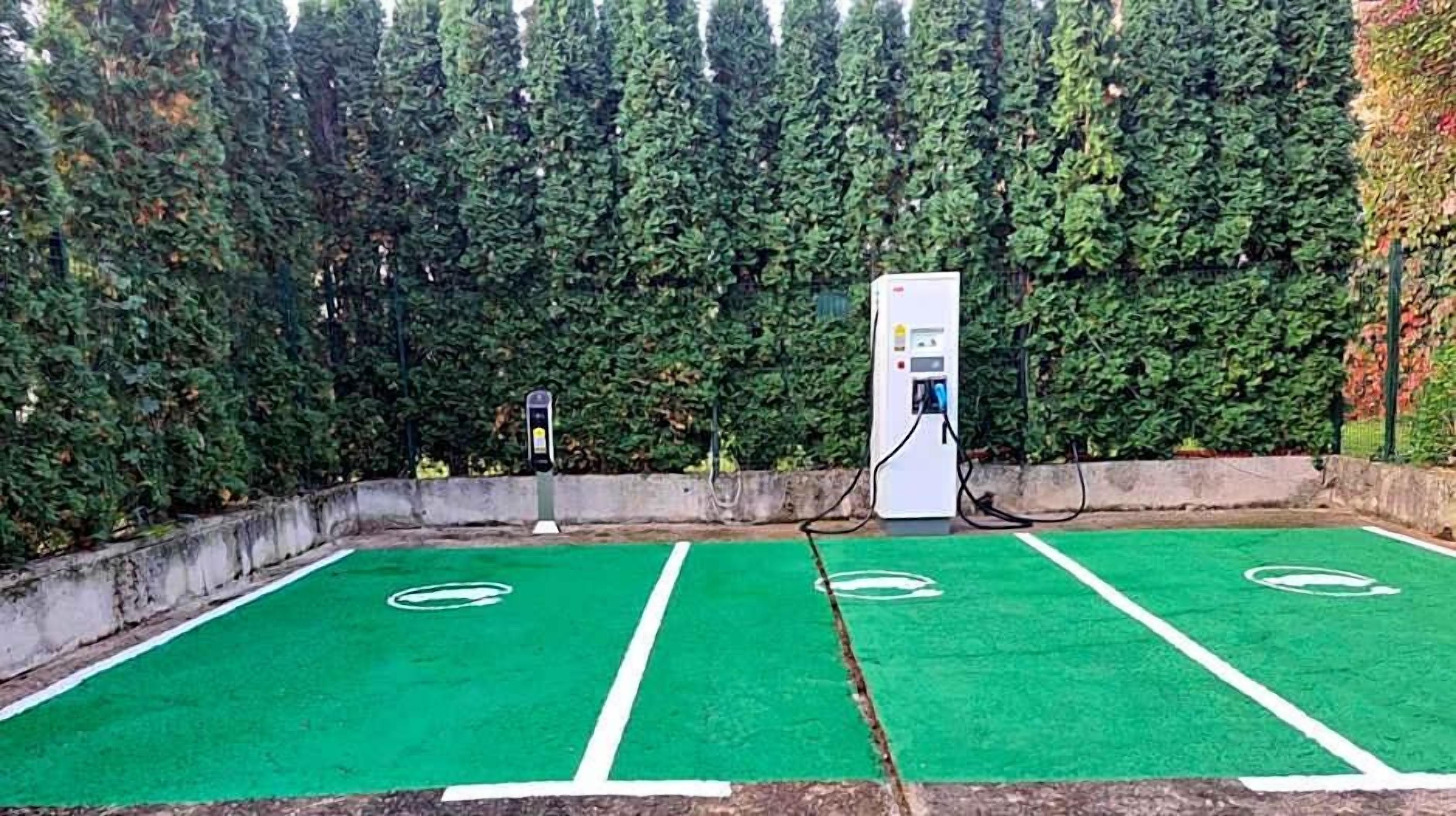 Un área de estacionamiento con estaciones de carga para vehículos eléctricos y espacios delimitados con pintura verde.