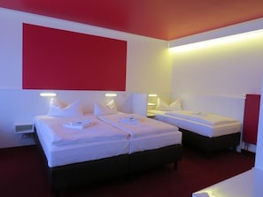 A hotel room with two beds, a red accent wall, and bedside lamps. - Ka Ka Hotel Garni (Warsow)