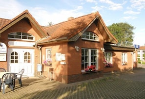 A brick building with a pitched roof, large windows, and a small outdoor seating area with chairs. - Ka Ka Hotel Garni (Warsow)