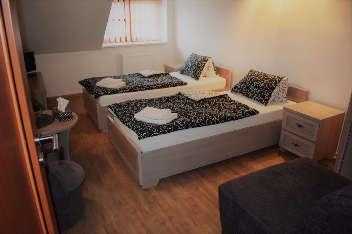 Habitación de hotel con dos camas, un escritorio pequeño, una silla y una ventana con persianas.