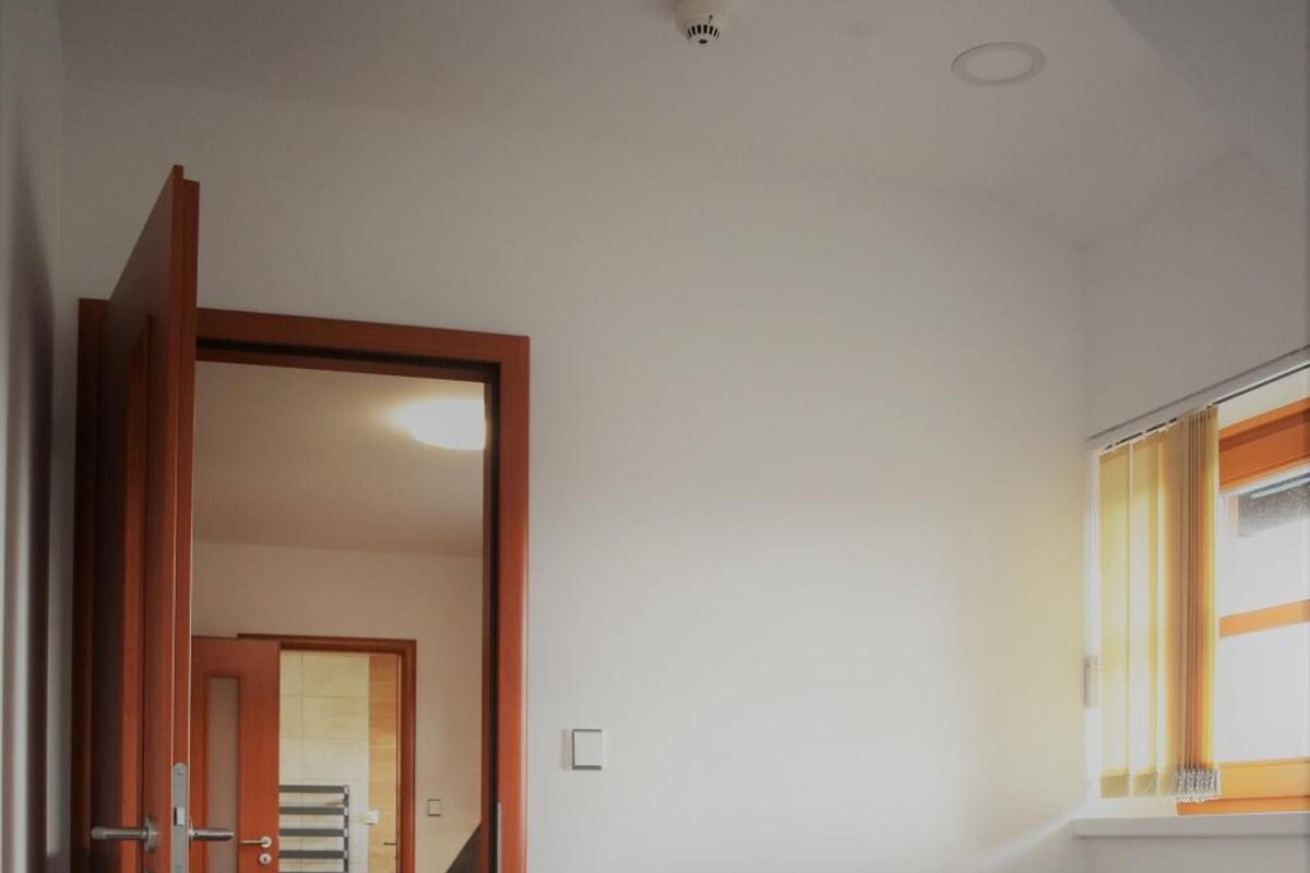 Un dormitorio con cama y cabecera de madera, una ventana con cortinas y un pasillo que conduce a otra habitación.