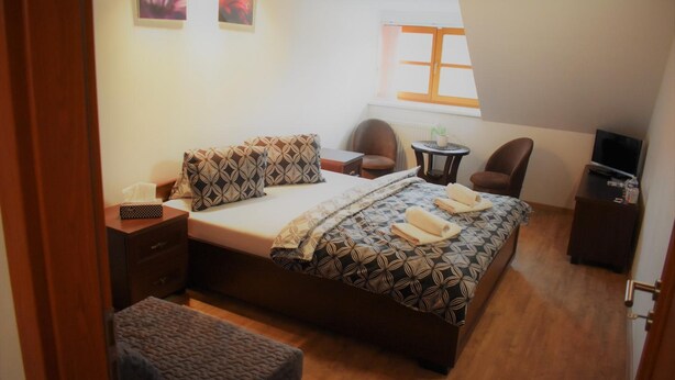 Un dormitorio con cama, dos sillas, una mesita, televisión y ventana.