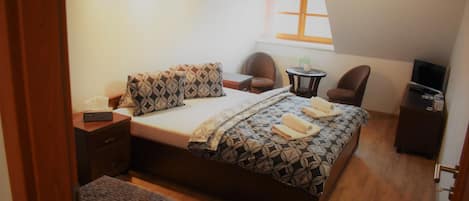 A bedroom with a bed, two chairs, a small table, a TV, and a window.