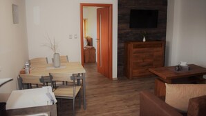 Una sala de estar moderna con comedor, piso de madera, un televisor de pantalla plana montado en una pared de piedra y un mueble de madera.