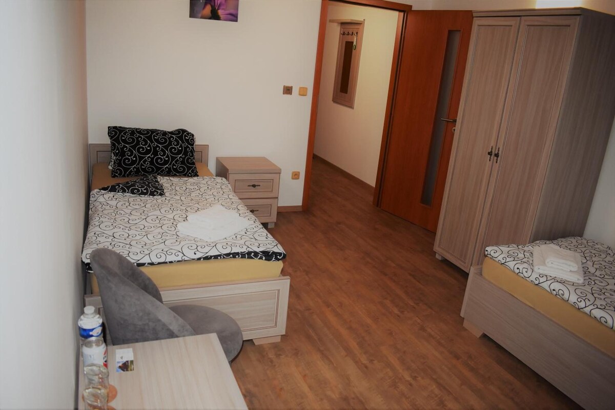 Un dormitorio con cama, escritorio, silla, armario y una pequeña mesa con una botella.