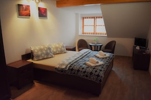 Un dormitorio con una cama, dos sillas, una mesita con una planta y un televisor sobre un mueble bajo.