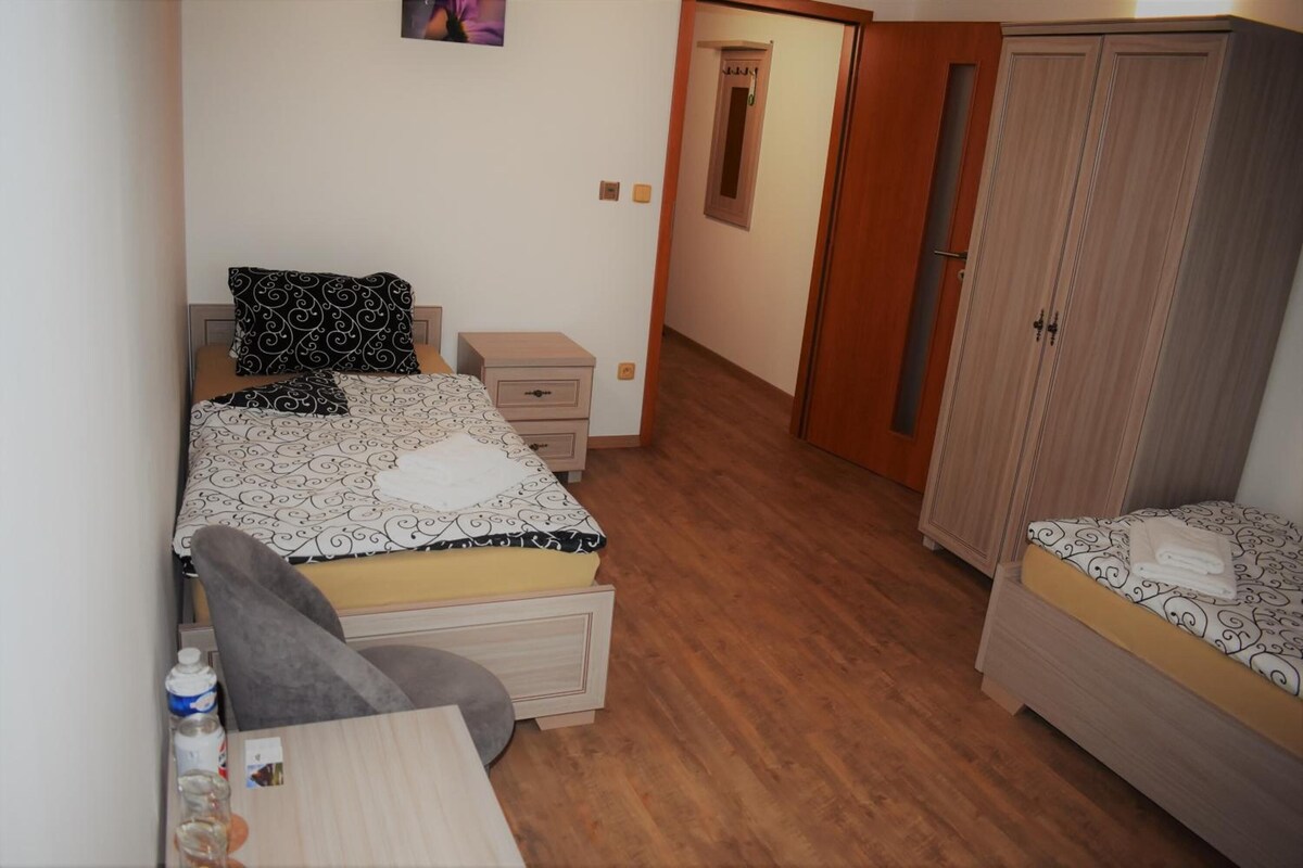 Un dormitorio con cama, escritorio, silla, armario y una pequeña mesa con una botella.