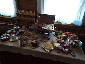 Una mesa de buffet con diversos alimentos, como pan, carnes, quesos y frutas.