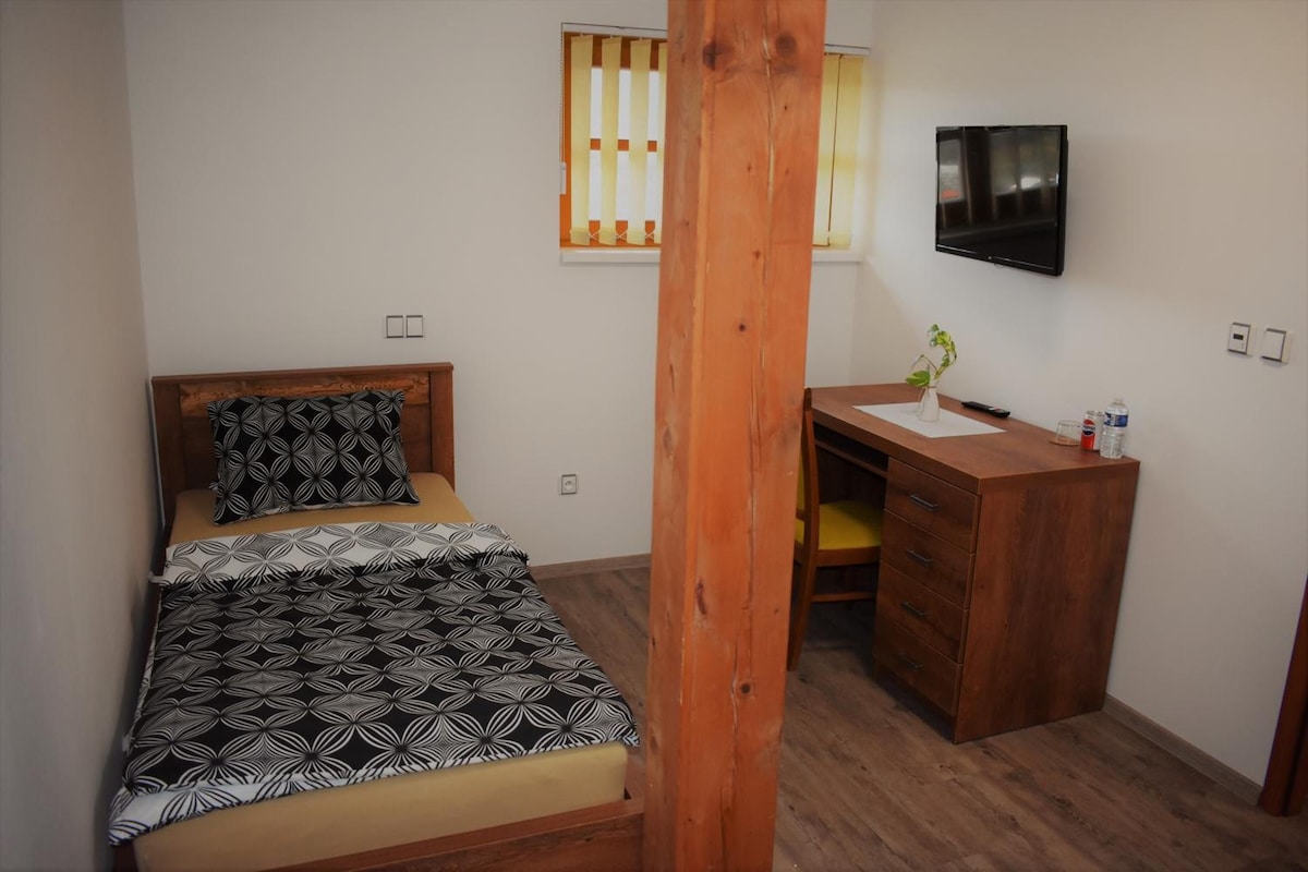 Un dormitorio con una cama, un escritorio de madera, un televisor y una ventana con persianas.