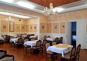 Un salón de banquetes con varias mesas y sillas, candelabros y cuadros en las paredes.