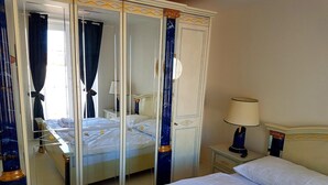 Habitación de hotel con una cama grande, una mesita de noche con lámpara, un espejo y un armario con cortina.