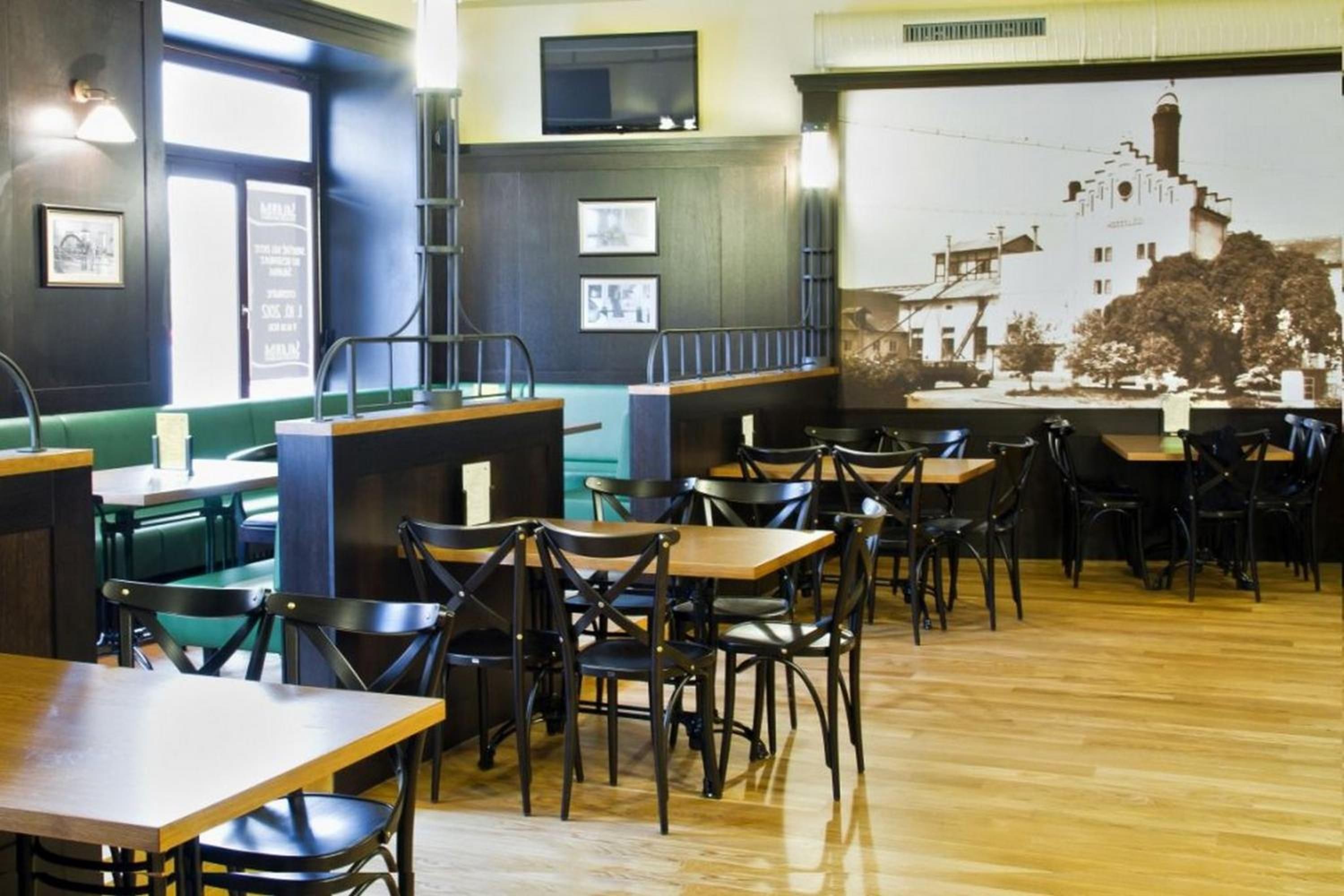 A restaurant interior with wooden tables and chairs, a green booth seating area, and a mural on the wall.
