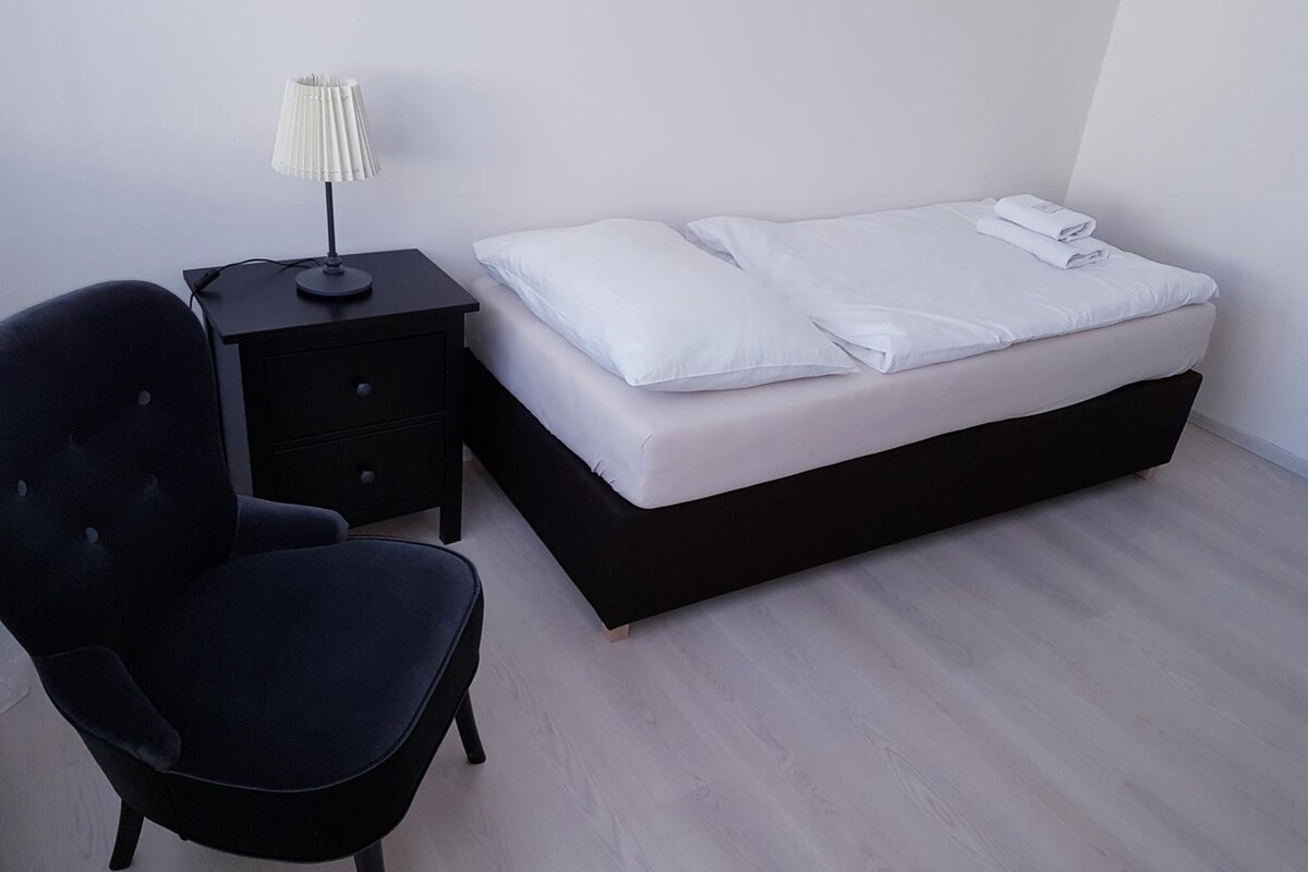 Un dormitorio con una cama, una silla, una mesita de noche y una lámpara.