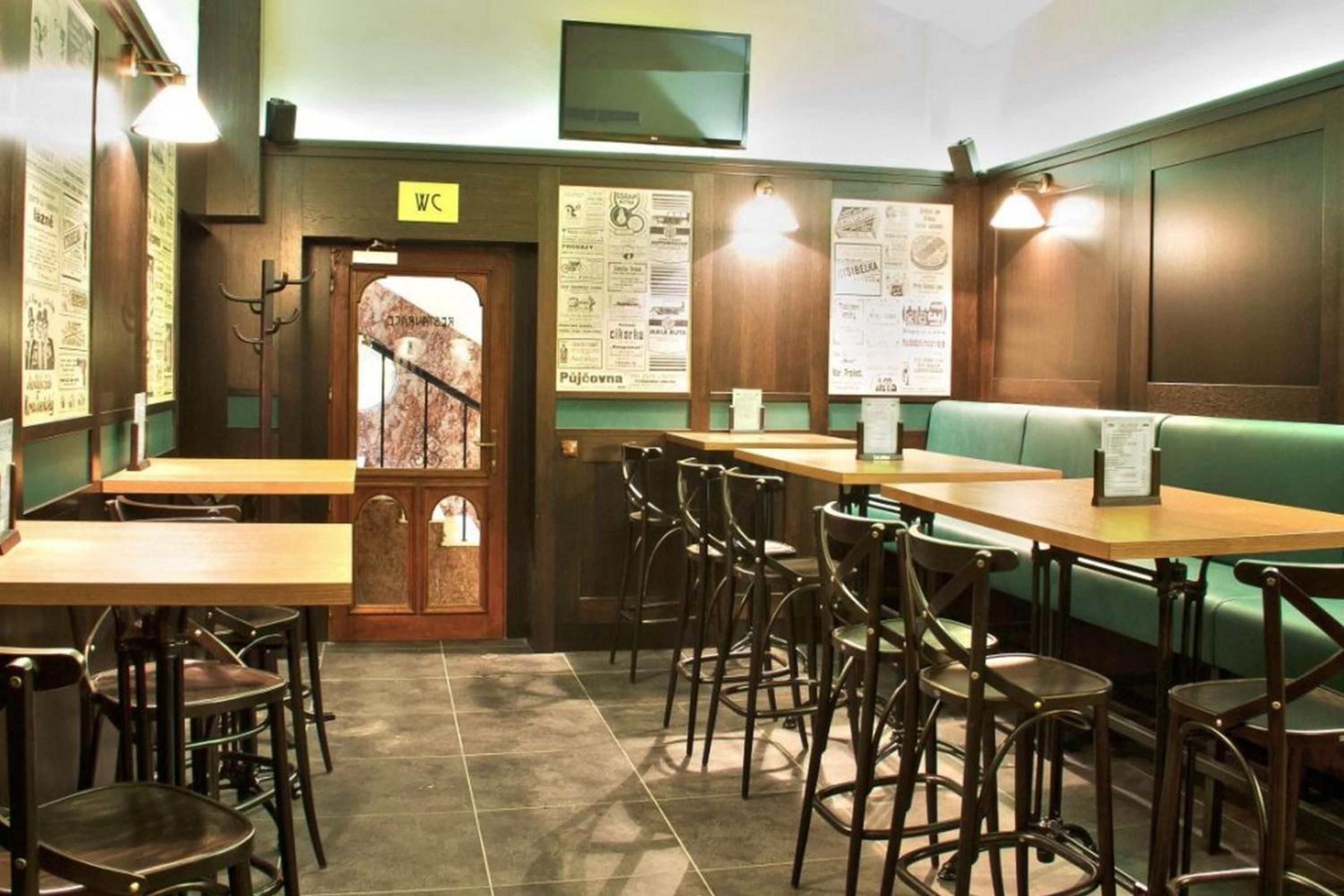 A restaurant interior with wooden tables and chairs, a green booth, and menu boards on the walls.