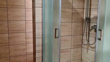 Una ducha con mampara de vidrio de diseño curvo, suelo de madera y pared con azulejos.