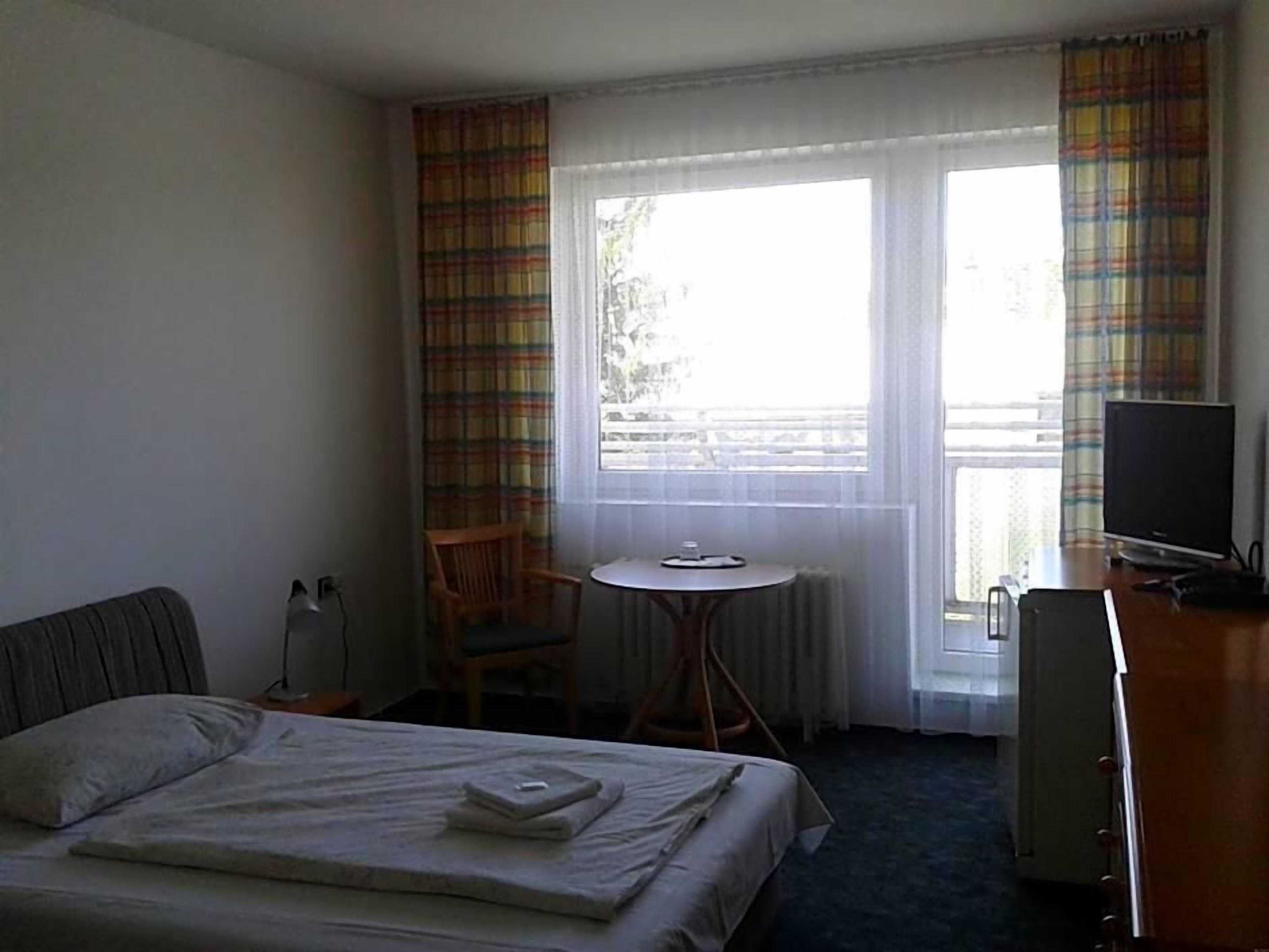 Een hotelkamer met een bed, bureau, stoel, televisie en raam met gordijnen.