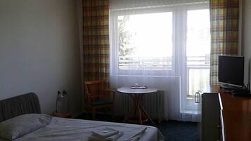 A hotel room with a bed, a desk, a chair, a television, and a window with curtains.