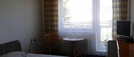 Habitación de hotel con cama, escritorio, silla, televisor y ventana con cortinas.