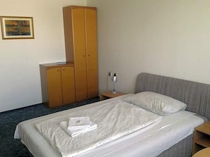 Una habitación de hotel con una cama, un armario, una mesita de noche y una lámpara.